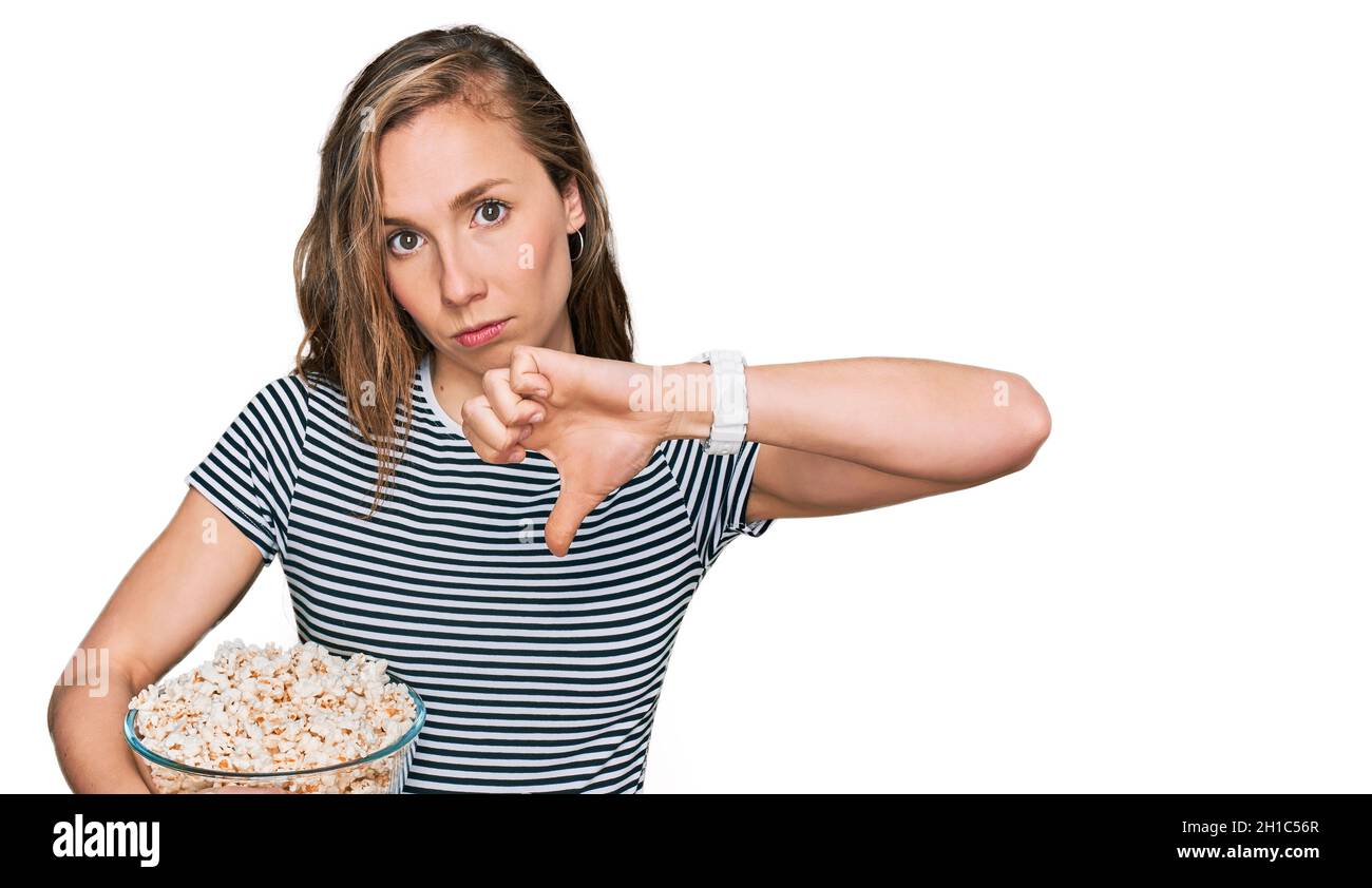 Young blonde woman eating popcorn with angry face, negative sign ...