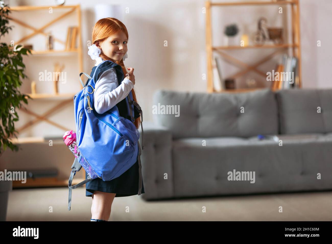 Portrait of little smiling girl, pupil wearing blue school uniform and big backpack. Being ready for school Stock Photo