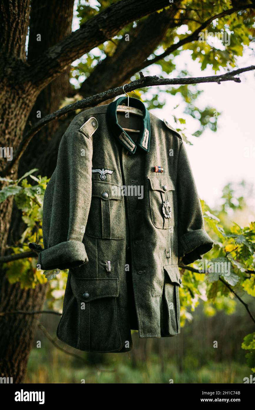 Coat Tunic Of World War II German Wehrmacht Infantry Soldier Hanging On A Hanger On Wood Outdoors In Camp. WWII WW2 Times. Uniform Of German Soldiers Stock Photo