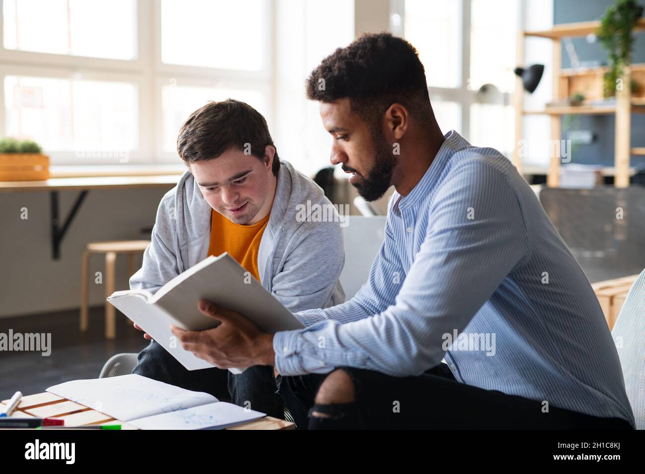 Young happy man with Down syndrome and his tutor studying indoors at school. Stock Photo