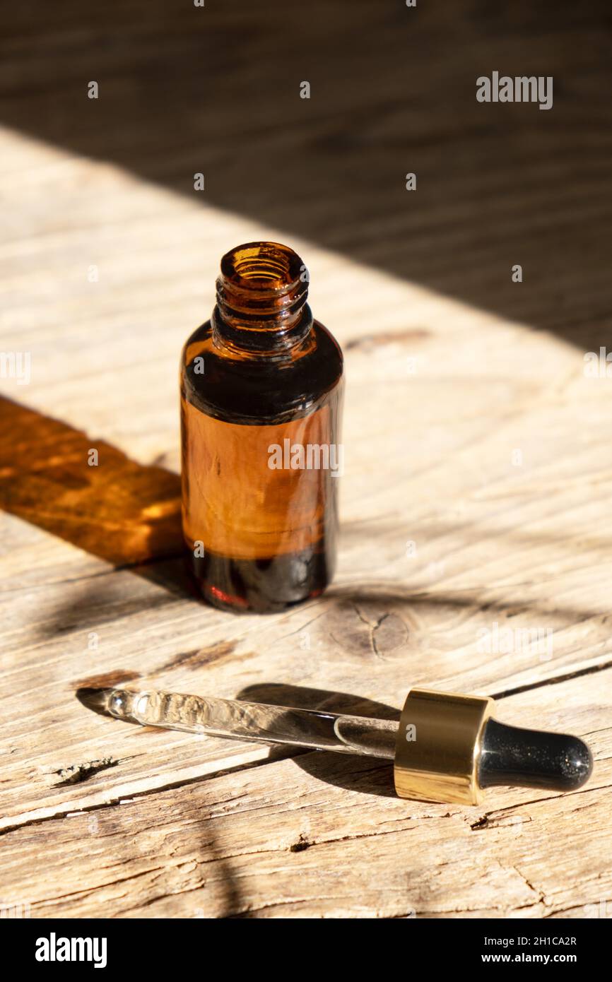 Dark amber glass bottle with dropper for oil, lotion or serum on a aged wooden background with a hard shadow of tropical palm leaves. Presentation of a cosmetic product. Layout of the beauty salon . Stock Photo