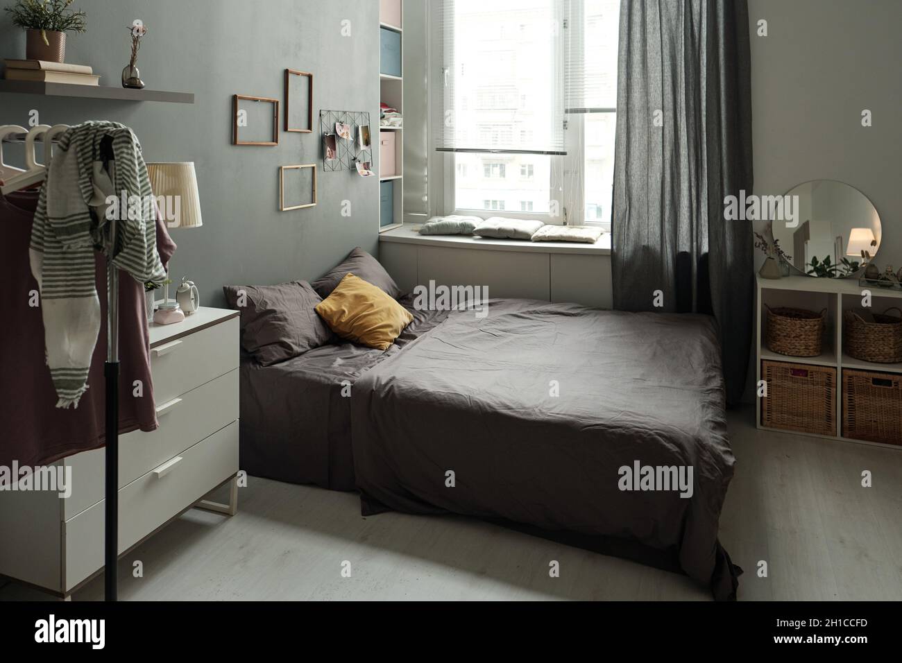 Interior of bedroom with double bed, furniture, rack for clothes, shelf and frames on wall and other stuff Stock Photo