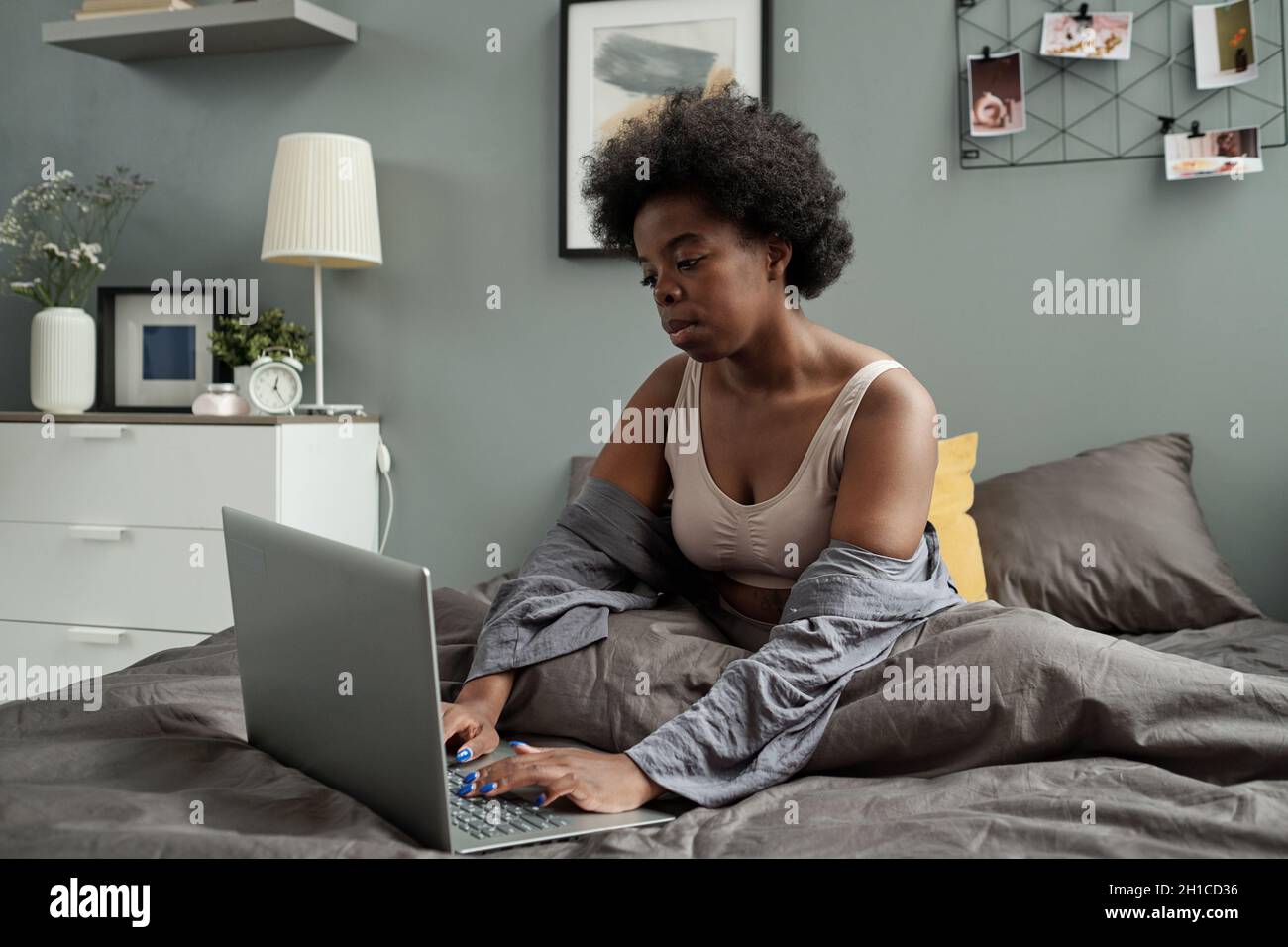 Young female freelancer with laptop sitting in bed after sleep and networking Stock Photo