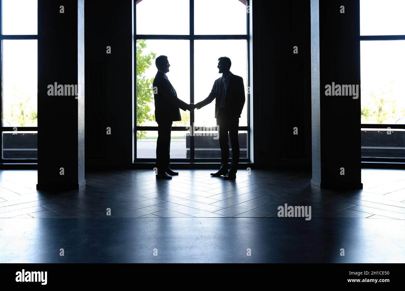 Full length view of businessmen shaking hands in office building. Stock Photo