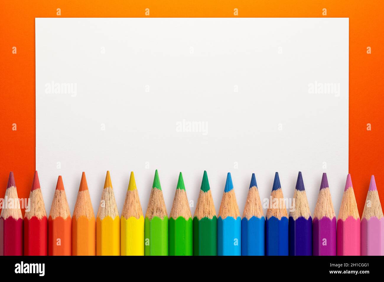 Frame made of color pencils and white paper on an orange background. Stock Photo