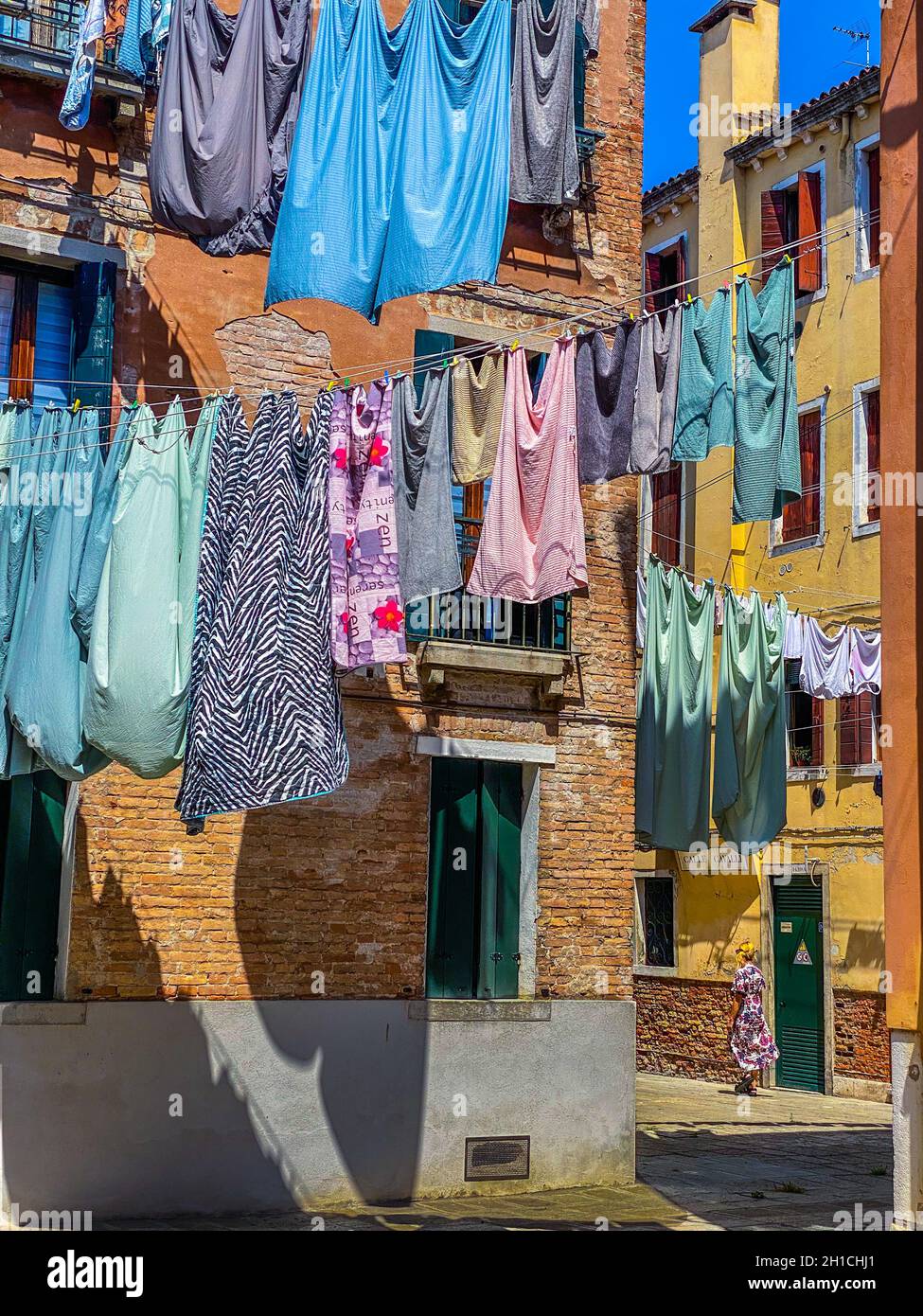 Woman walking under Hanging clothes put to dry on a small traditional street of Venice, Italy. Travel background Stock Photo