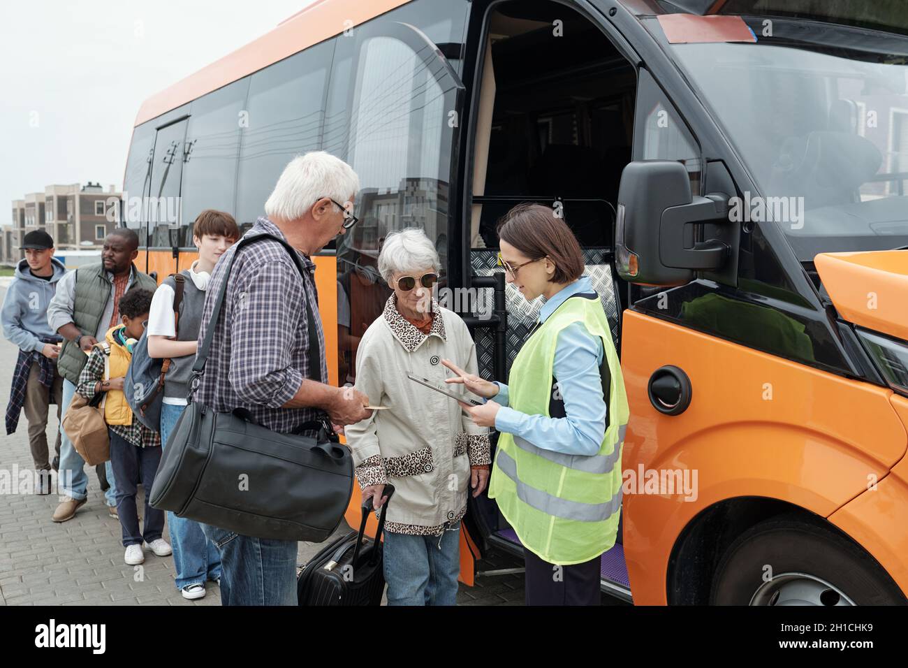 Bus conductor checking tickets of intercultural passengers standing in line along vehicle Stock Photo