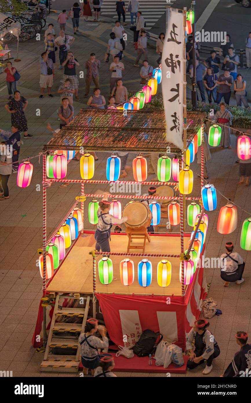 View of the square in front of the Nippori train station decorated for the Obon festival with a yagura tower illuminated with paper lanterns where a g Stock Photo