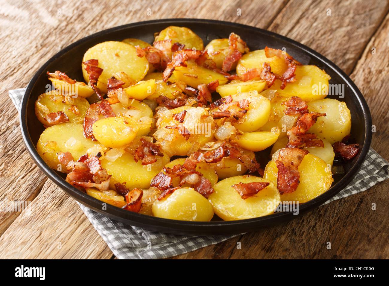 Delicious Fried Potato Bratkartoffeln With Bacon and Onion close up in the plate on the table. Horizontal Stock Photo
