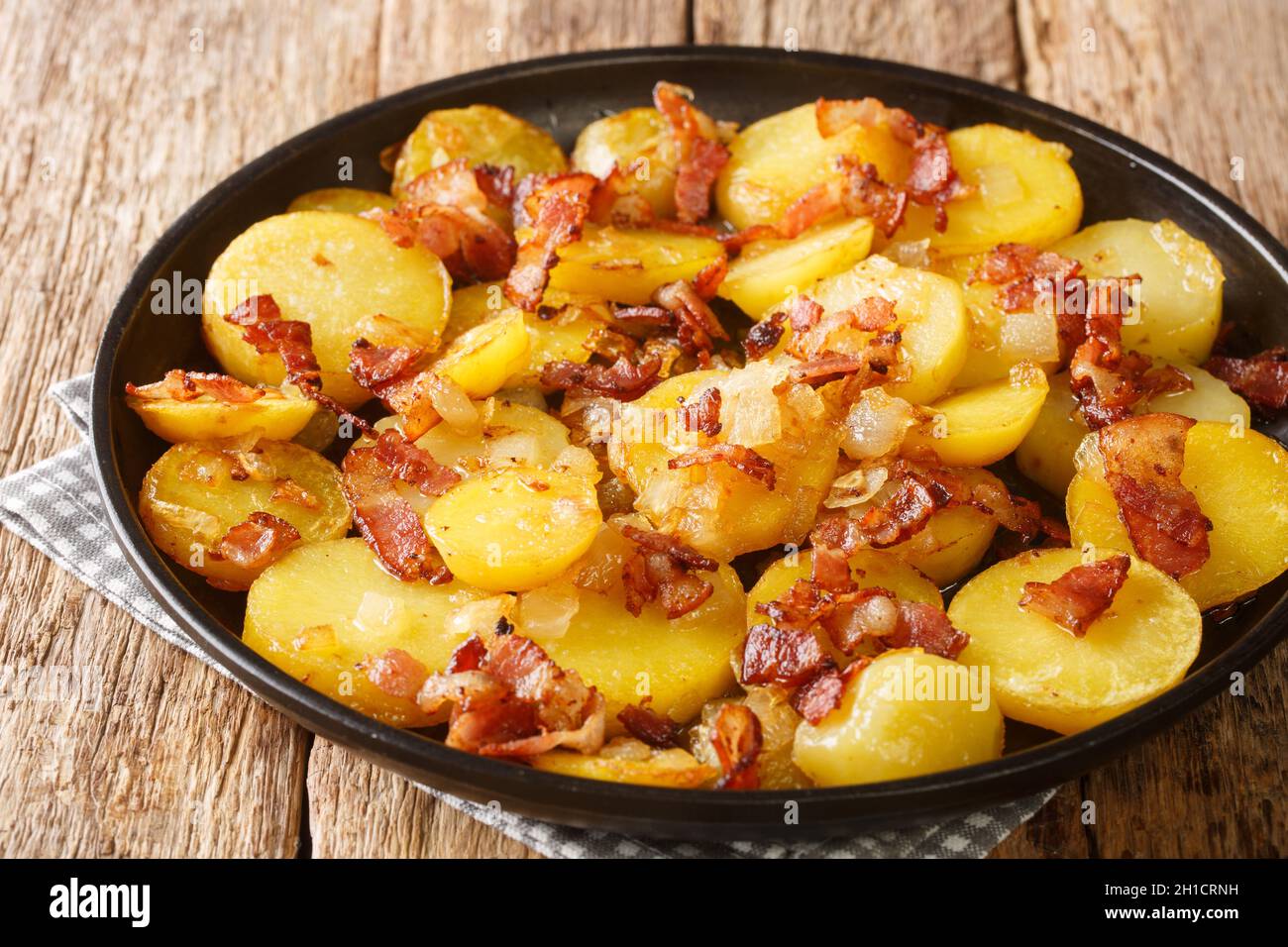 Bratkartoffeln German Cottage Fries With Bacon and Onion close up in the plate on the table. Horizontal Stock Photo