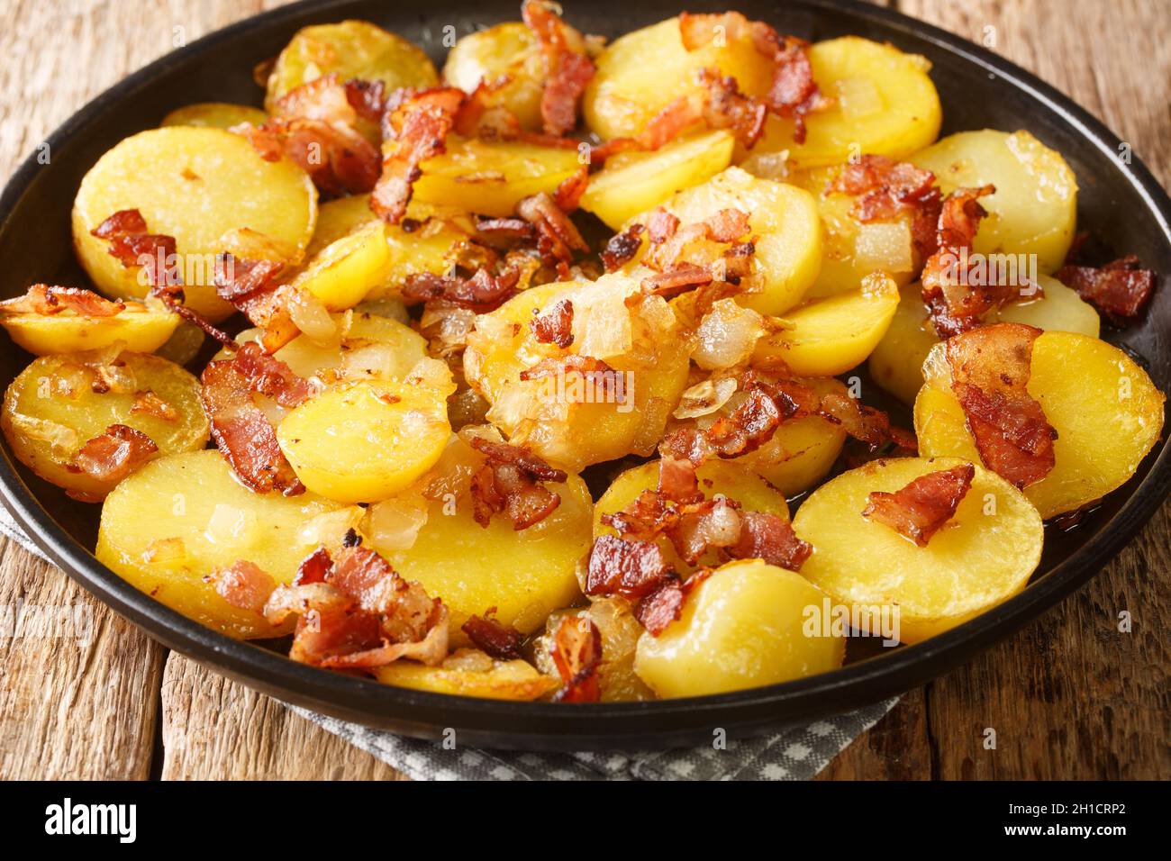 German Pan Fried Potatoes or Bratkartoffeln With Bacon and Onion close up in the plate on the table. Horizontal Stock Photo