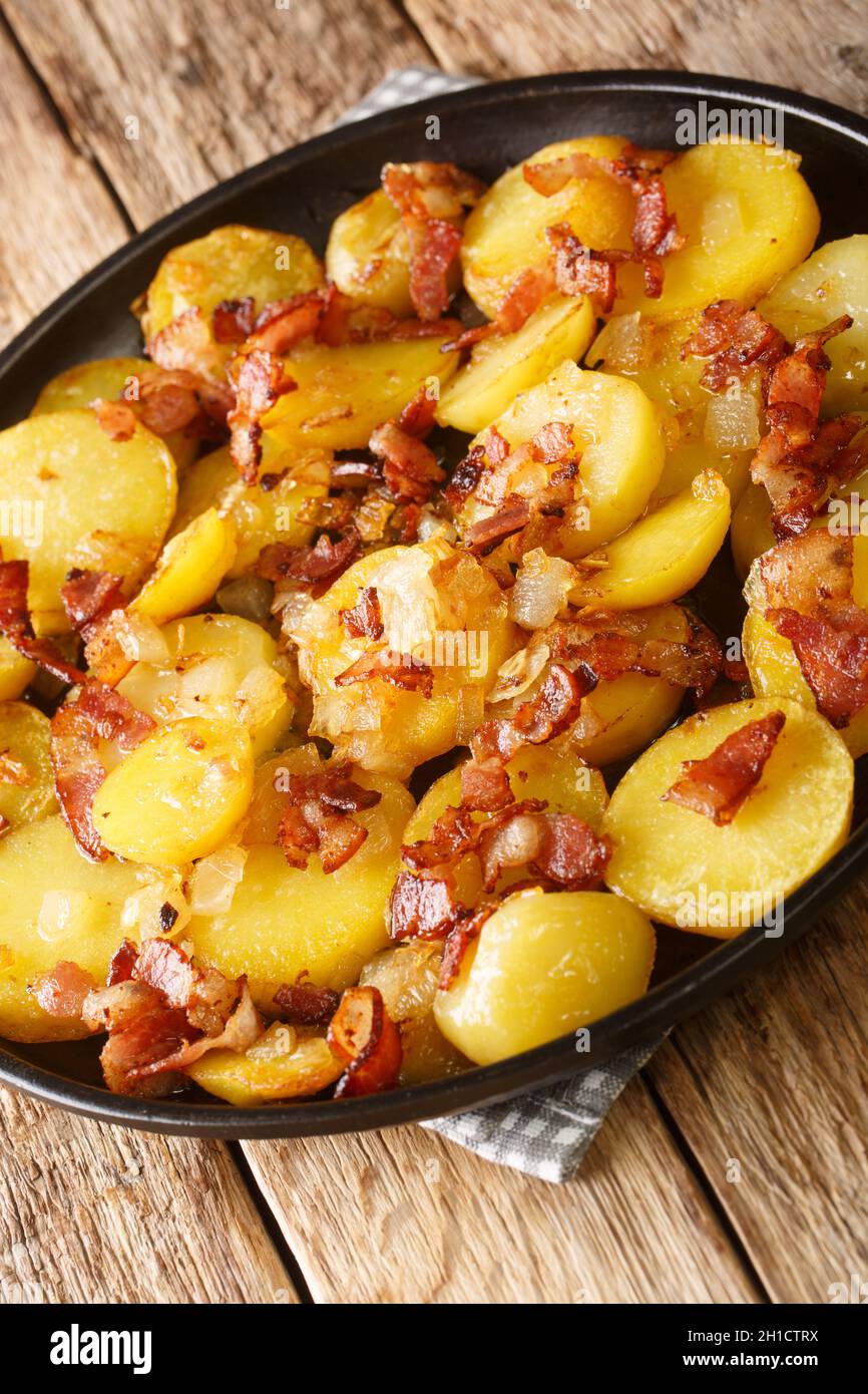 Bratkartoffeln German Cottage Potatoes With Bacon and Onion close up in the plate on the table. Vertical Stock Photo