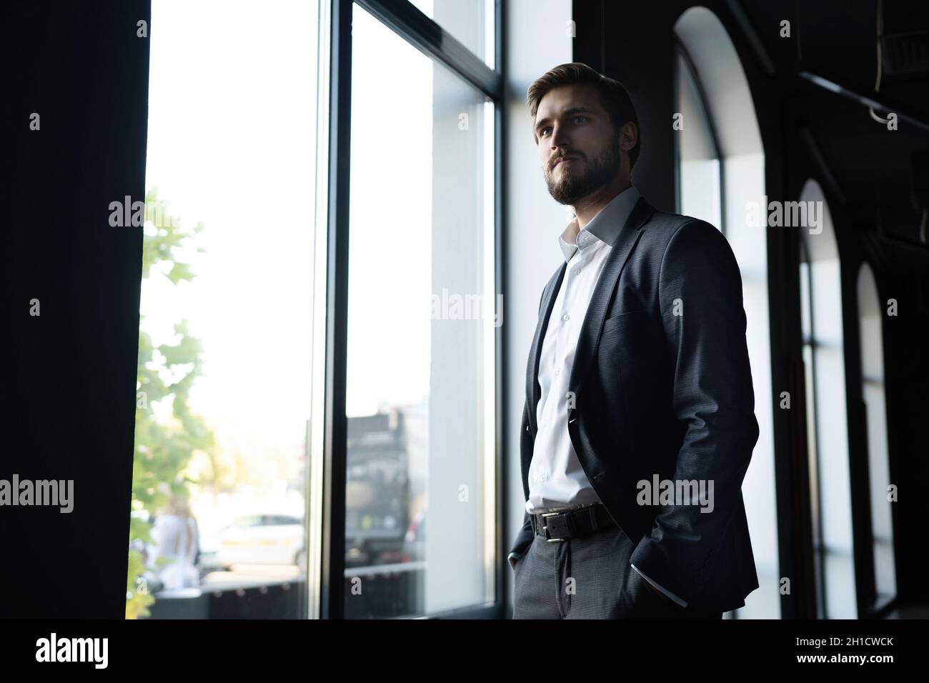 Confident young businessman looking at camera while standing near the window an office building. Stock Photo