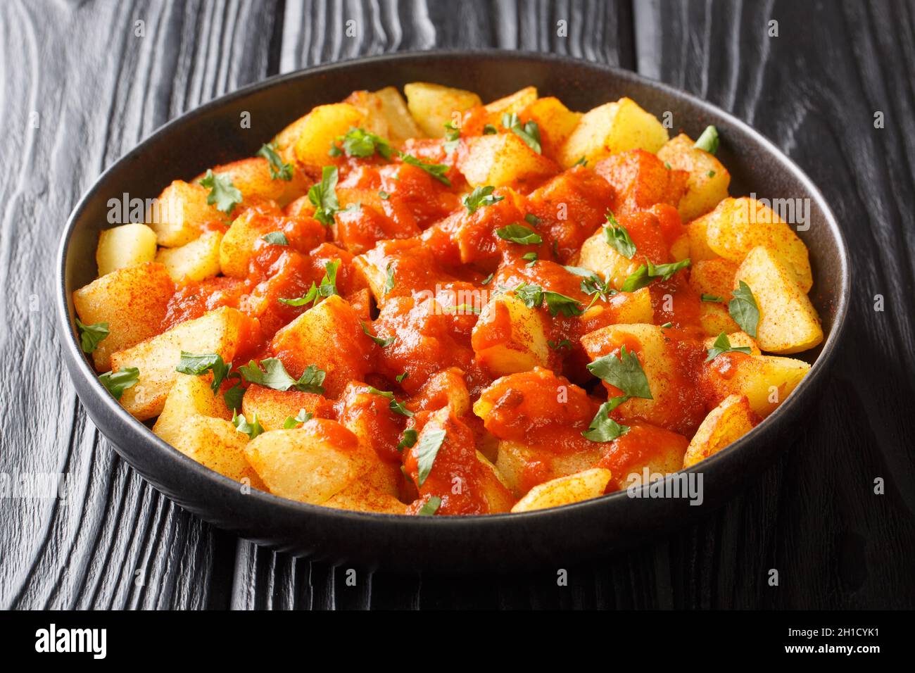 Patatas bravas or potatoes in bravas sauce are a classic Spanish tapas dish close up in the plate on the table. Horizontal Stock Photo