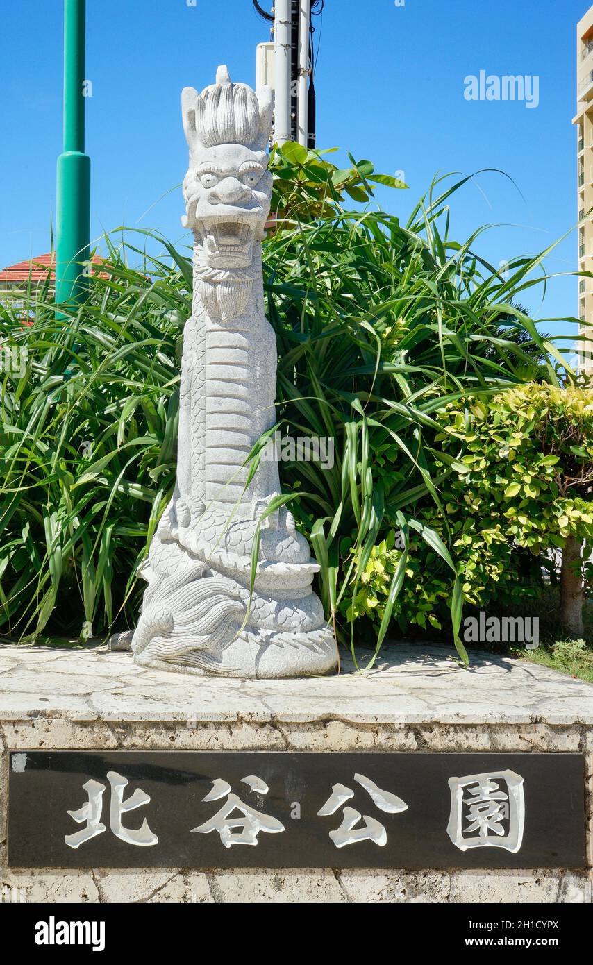 Okinawan Ryukyu dragon stone sculpture and stone sign where is inscribed Chatan Park in japanese on the sunset beach in the American Village of Okinaw Stock Photo