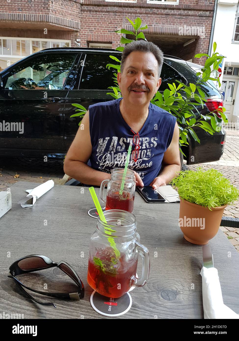 LÜNEBURG, NIEDERSACHSEN, GERMANY - JULI 27, 2018: Man is sitting in the beer garden of a restaurant in Lueneburg with mobile phone in hand. Looking at Stock Photo