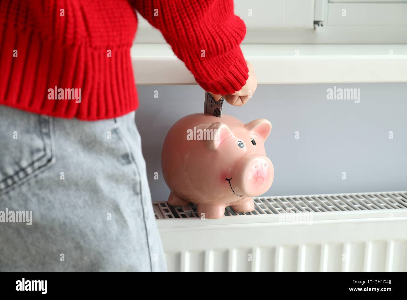 Heating season concept with a girl putting a banknote in a piggy bank. Stock Photo