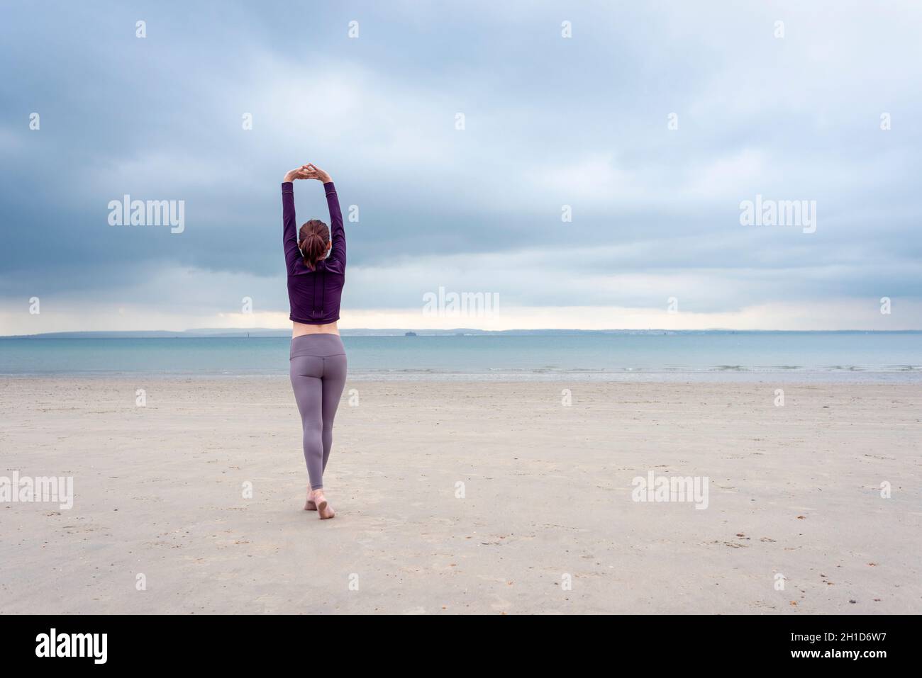 Woman stretching keeping fit arms up  by the sea, rearview. Stock Photo