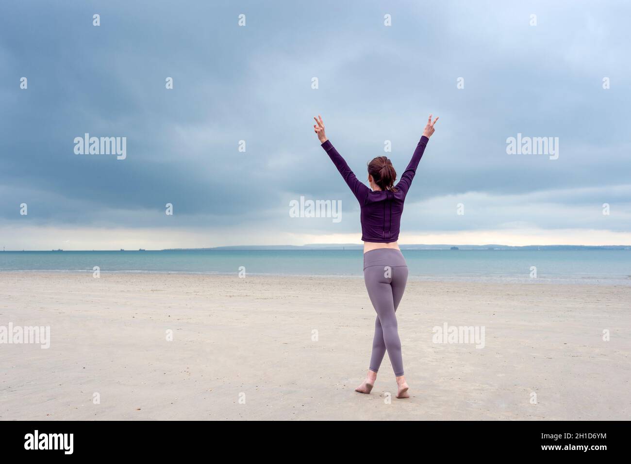Young woman in sportswear is standing and lifting up arms for freedom on the beach Stock Photo