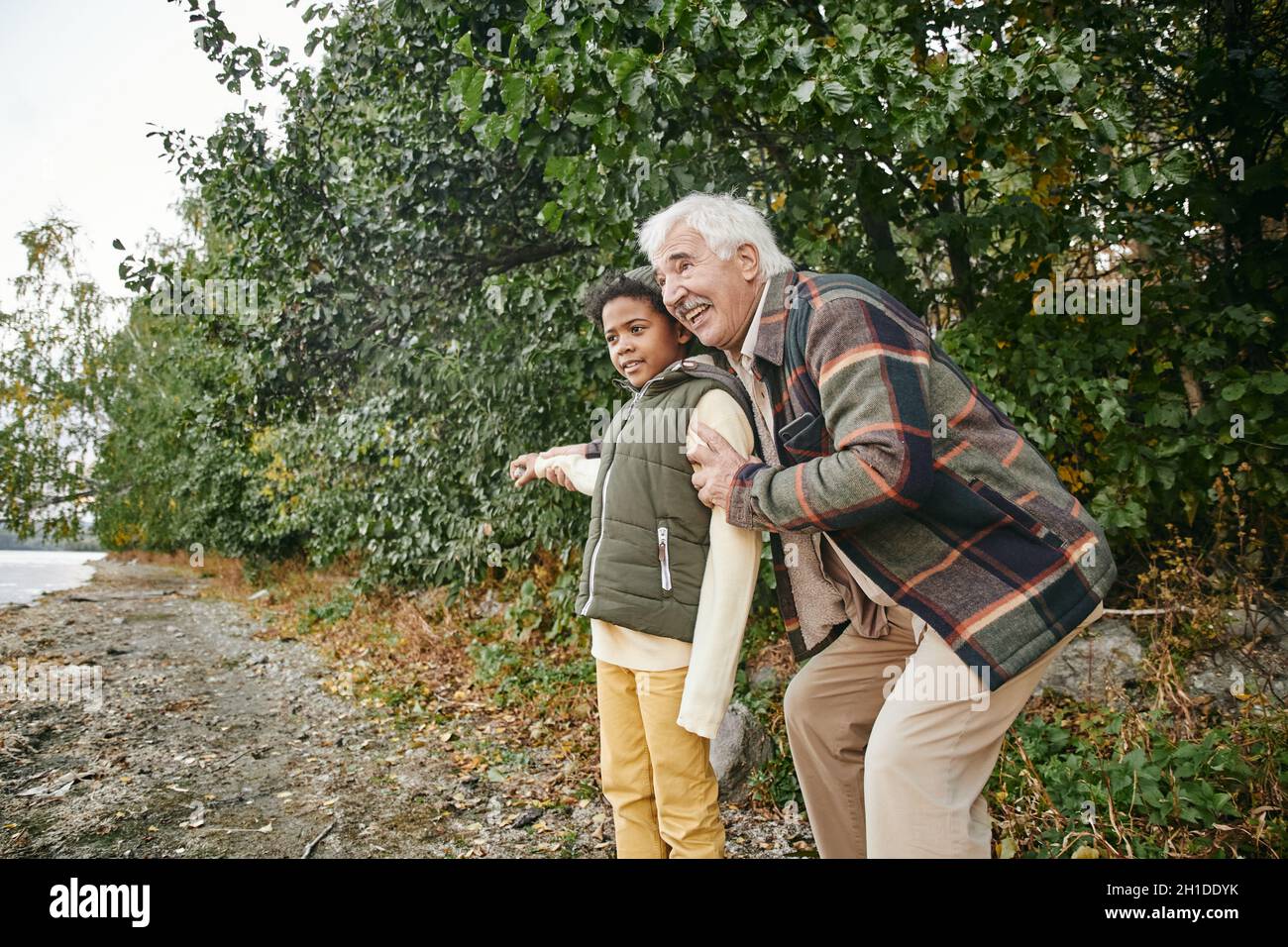 Happy grandfather spending funny time together with his gfrandson in the forest during autumn day Stock Photo