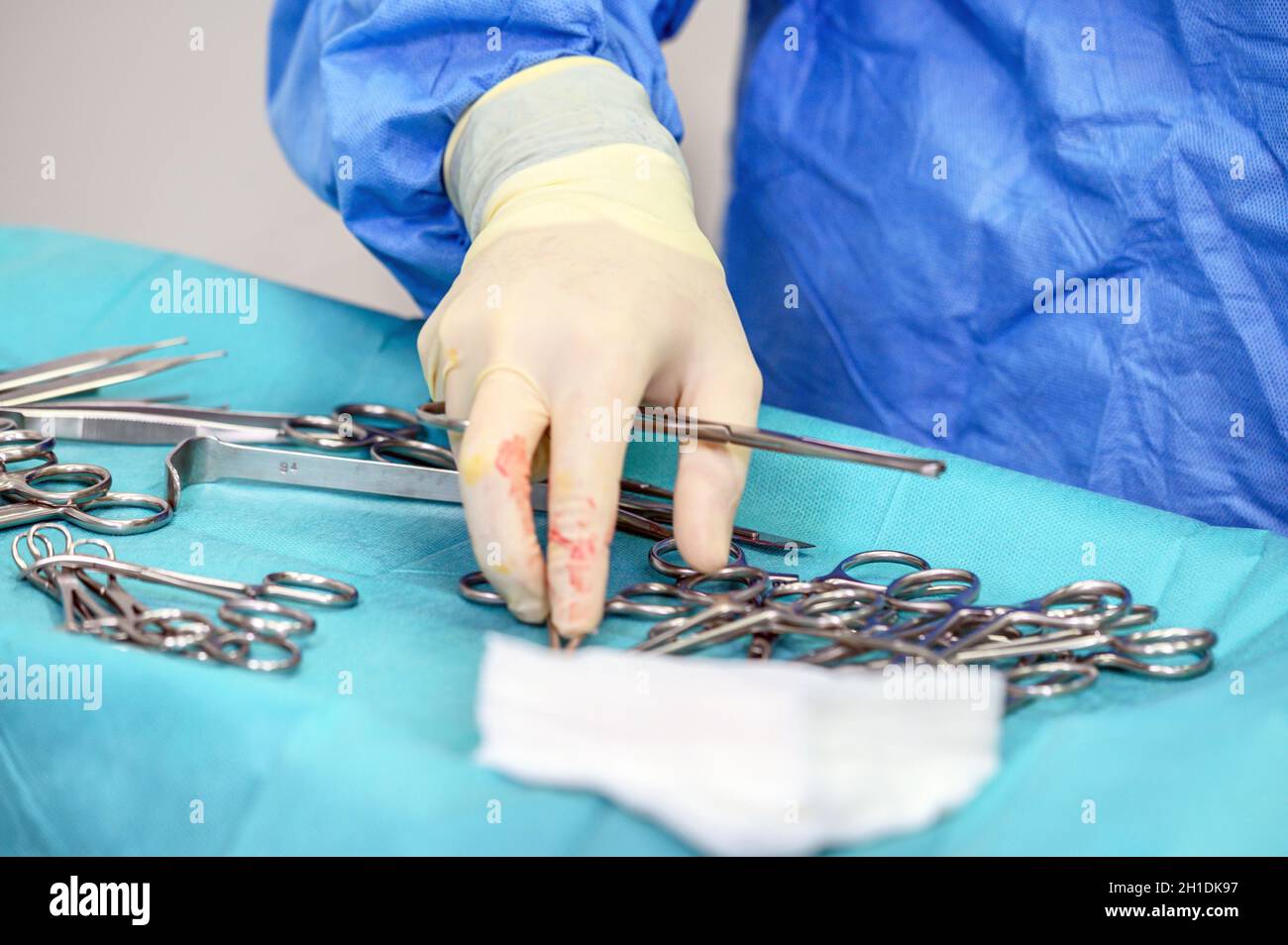 Close-up of scrub nurse taking medical instruments for operation with colleagues performing in background . Stock Photo