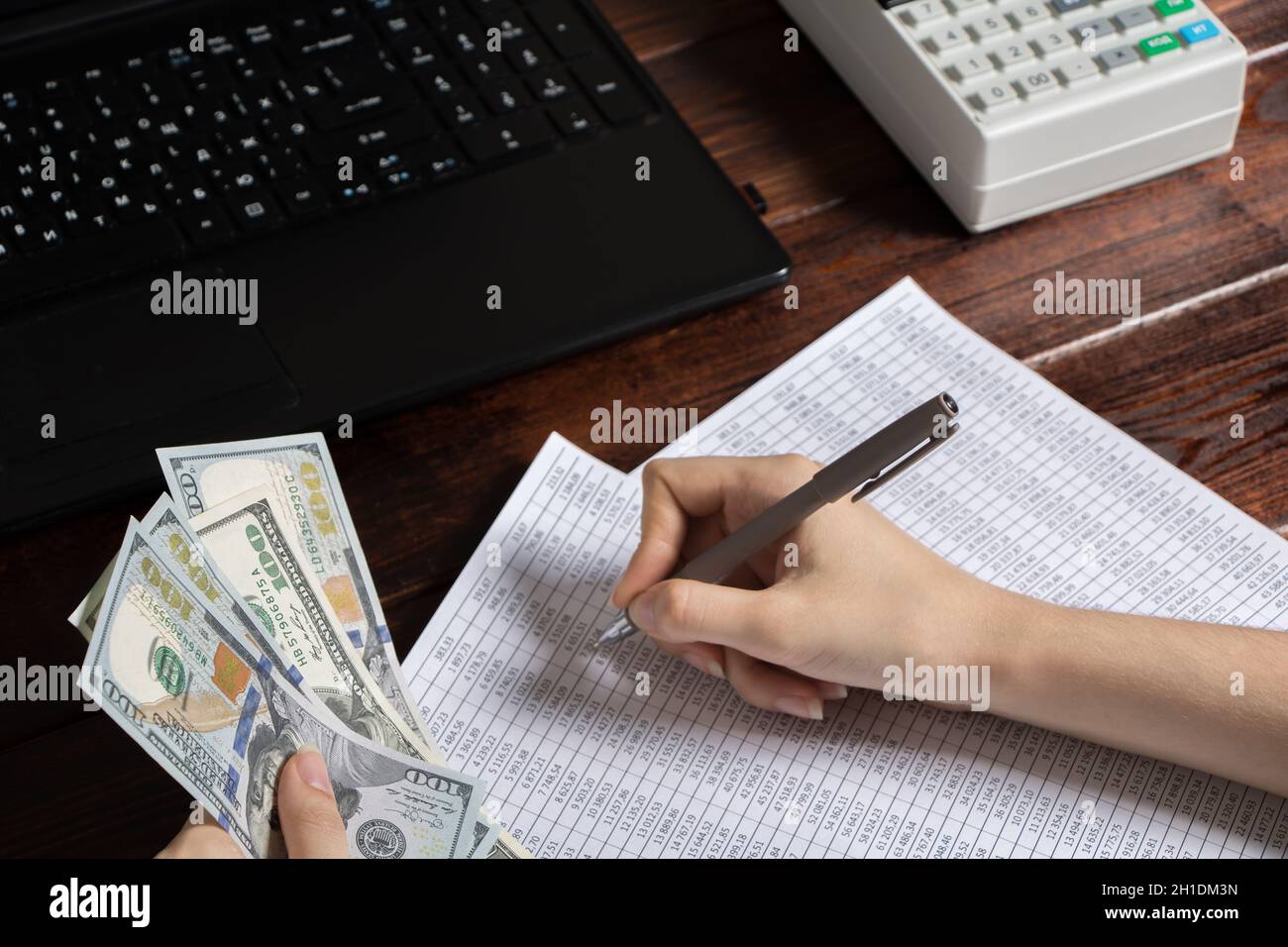 Obligation to pay wages and debts in the company.A cashier holds money dollars over an office work space with documents, a cash register, a phone, and Stock Photo