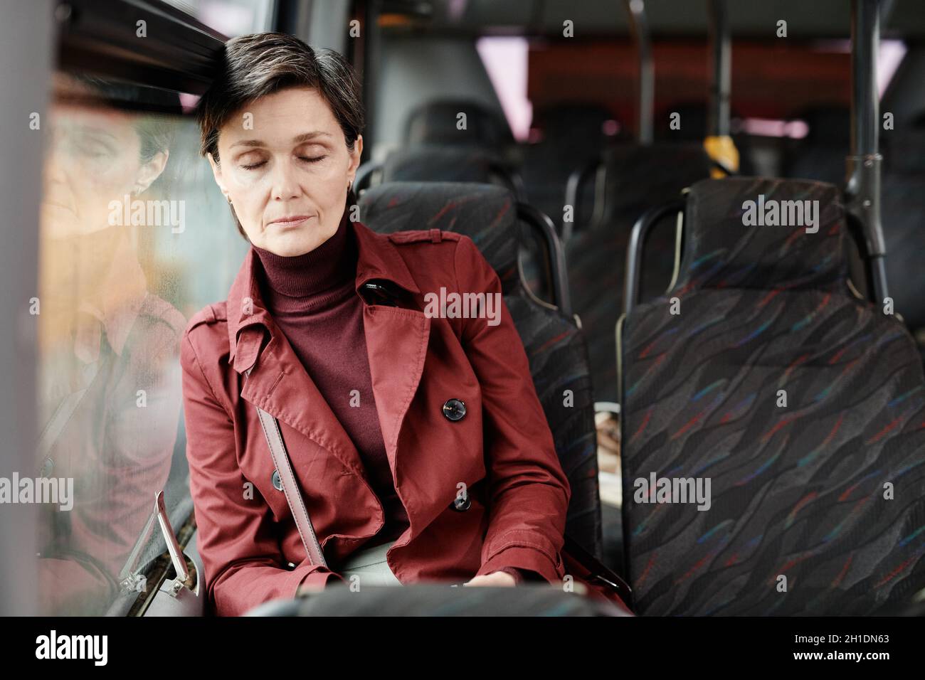 Portrait of elegant mature woman sleeping on bus while traveling by public transport in city, copy space Stock Photo