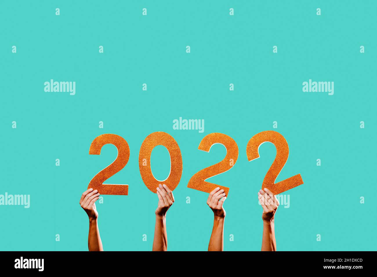 men hands holding some golden three-dimensional numbers forming the number 2022, as the new year, on a blue background with some blank space on top Stock Photo