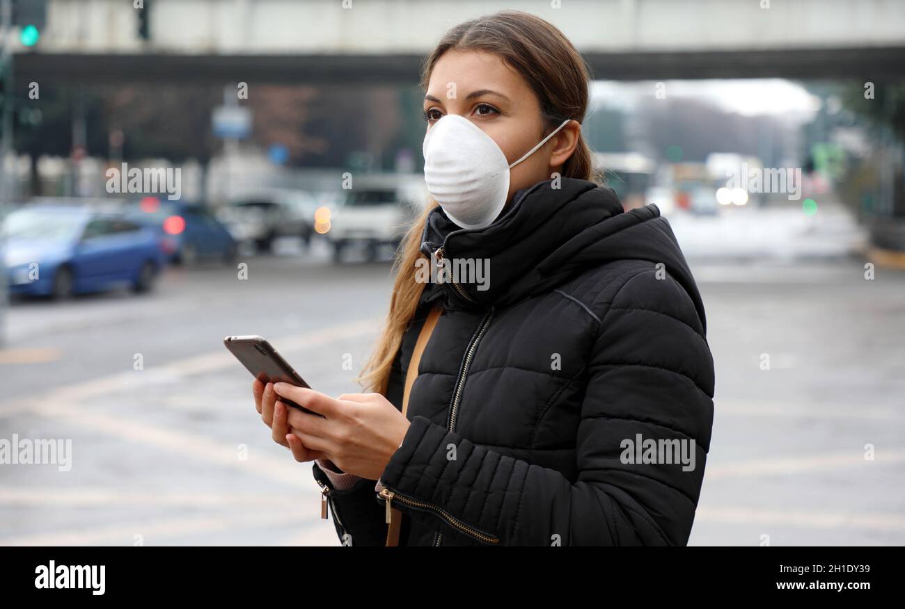 COVID-19 Pandemic Coronavirus Mobile Application - Young Woman Wearing Face Mask Using Smart Phone App in City Street to Aid Contact Tracing in Respon Stock Photo