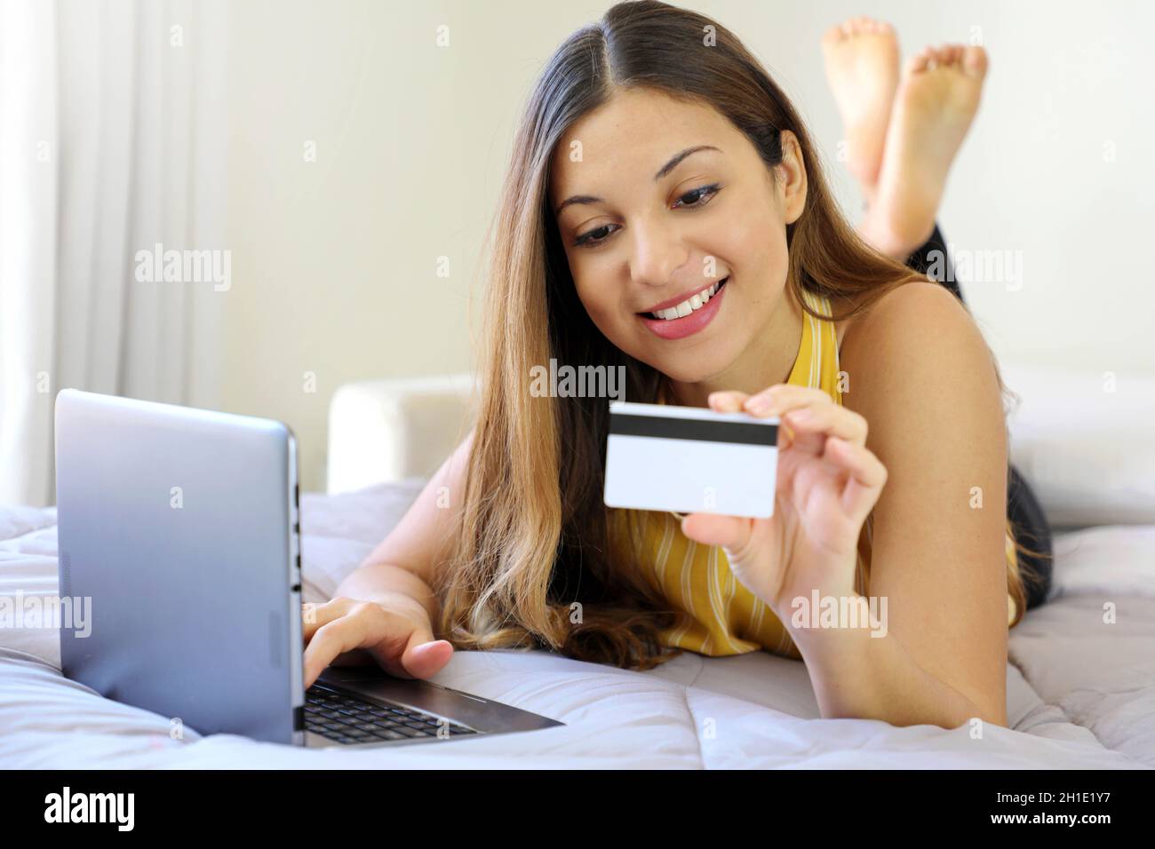 Smiling relaxed young woman lying on bed reading her credit card number