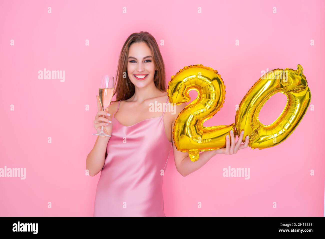 Young happy woman holds gold foil balloon and glass of champagne on pink background. BIRTHDAY PARTY Stock Photo