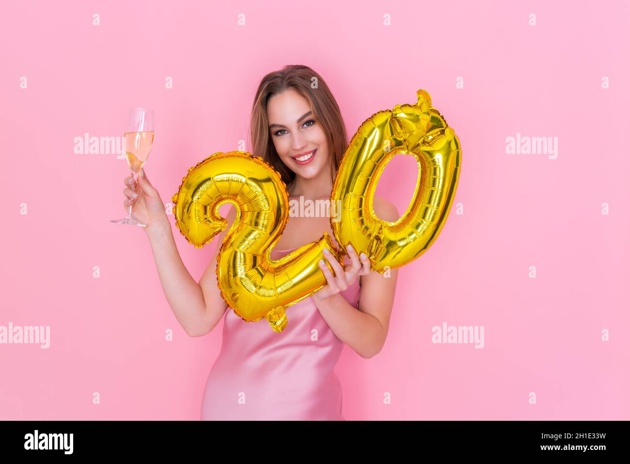 Young smiling woman holds gold foil balloon and glass of champagne on pink background BIRTHDAY PARTY Stock Photo