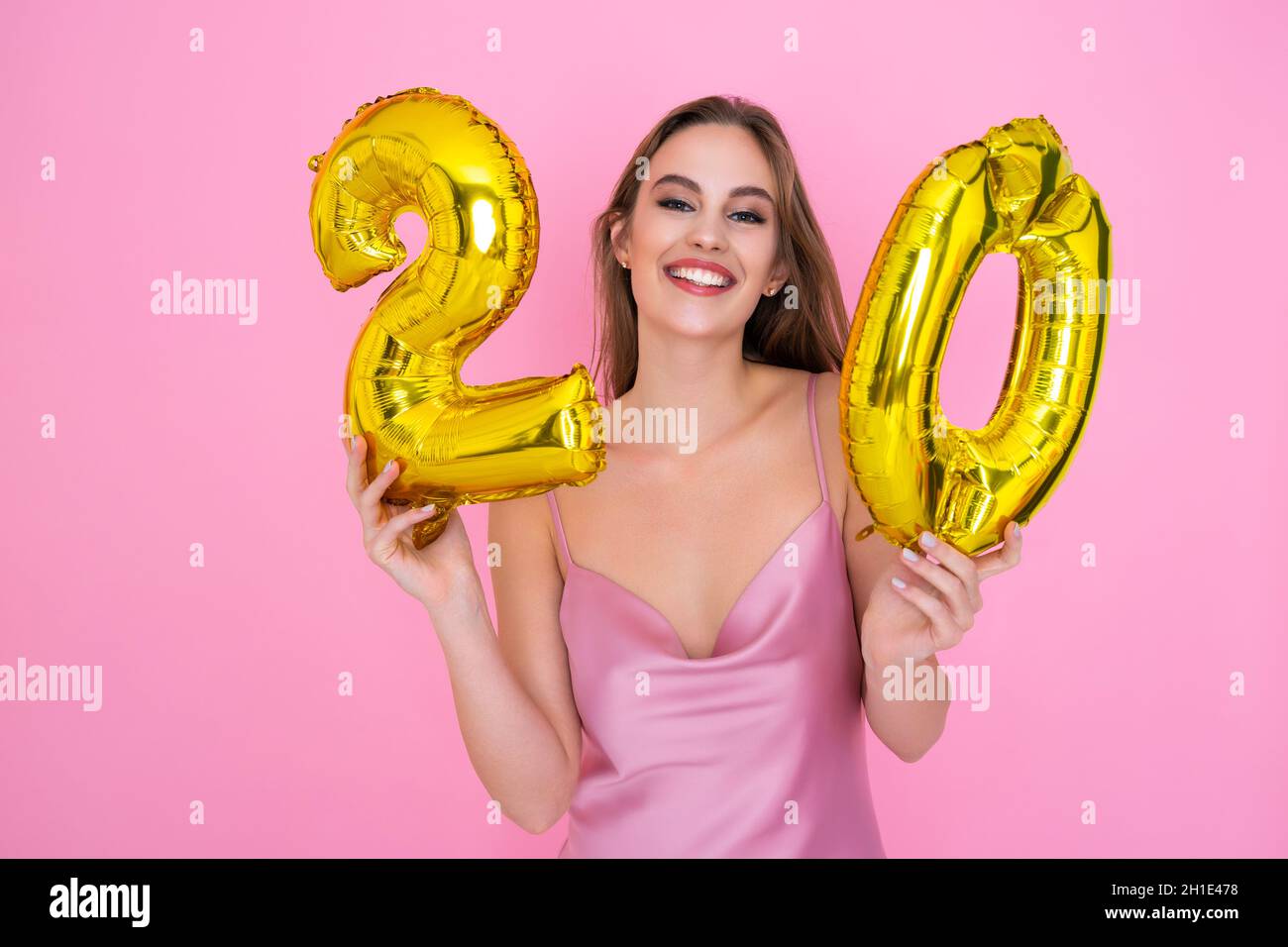 Young teenager smiling girl holds gold foil balloon on pink background. BIRTHDAY PARTY concept Stock Photo