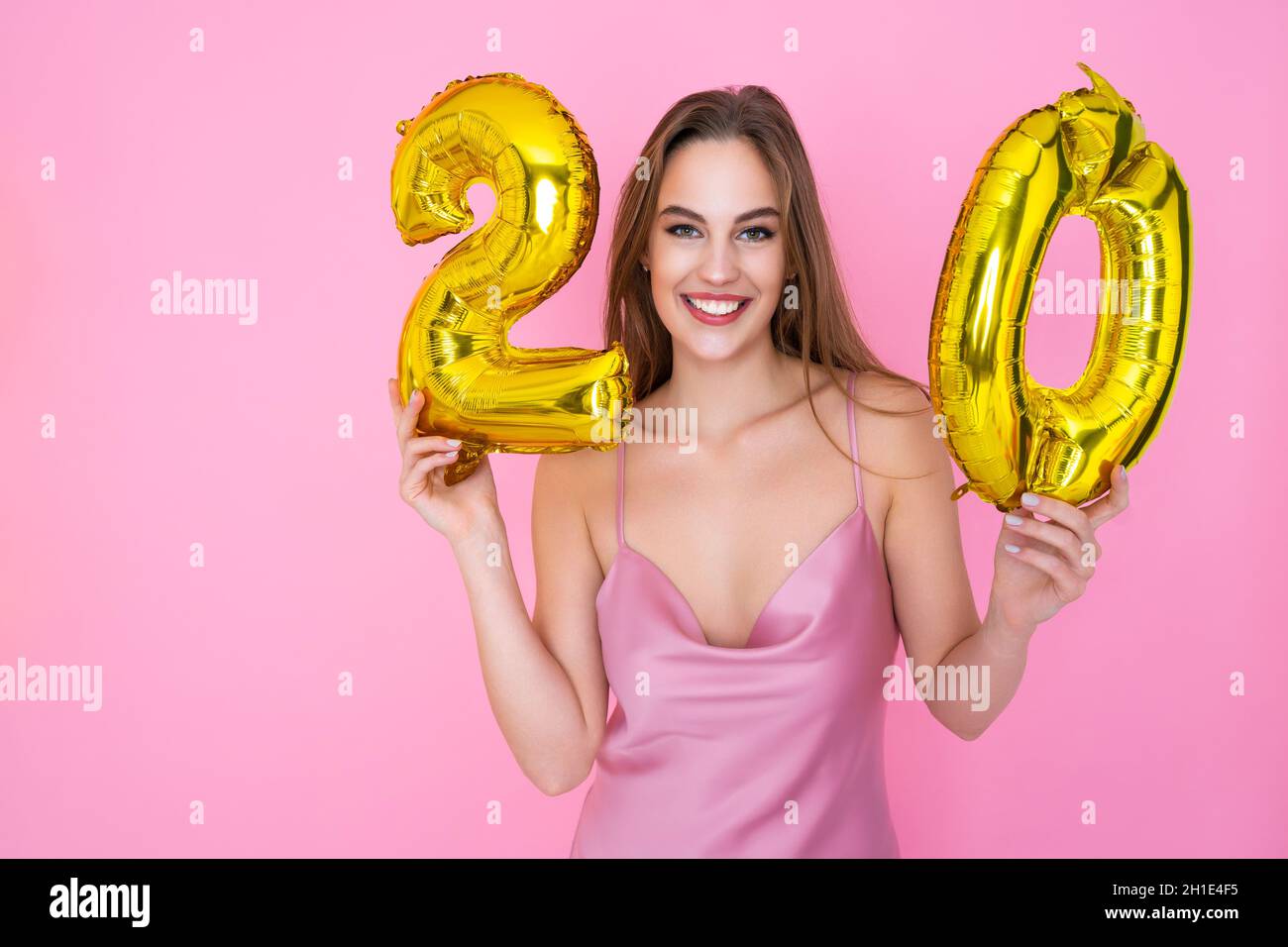 Young teenager cheerful girl holds gold foil balloon on pink background. BIRTHDAY PARTY concept Stock Photo