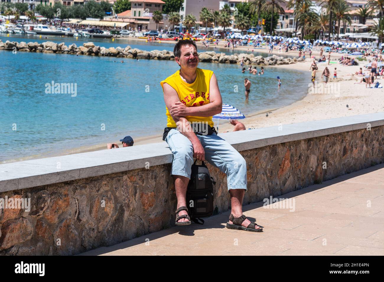 Paguera, MALLORCA, SPAIN - JULY 02, 2016: Paguera, Mallorca, Spain - July 02, 2016: A man sitting in the sunshine on a wall in the background pine for Stock Photo