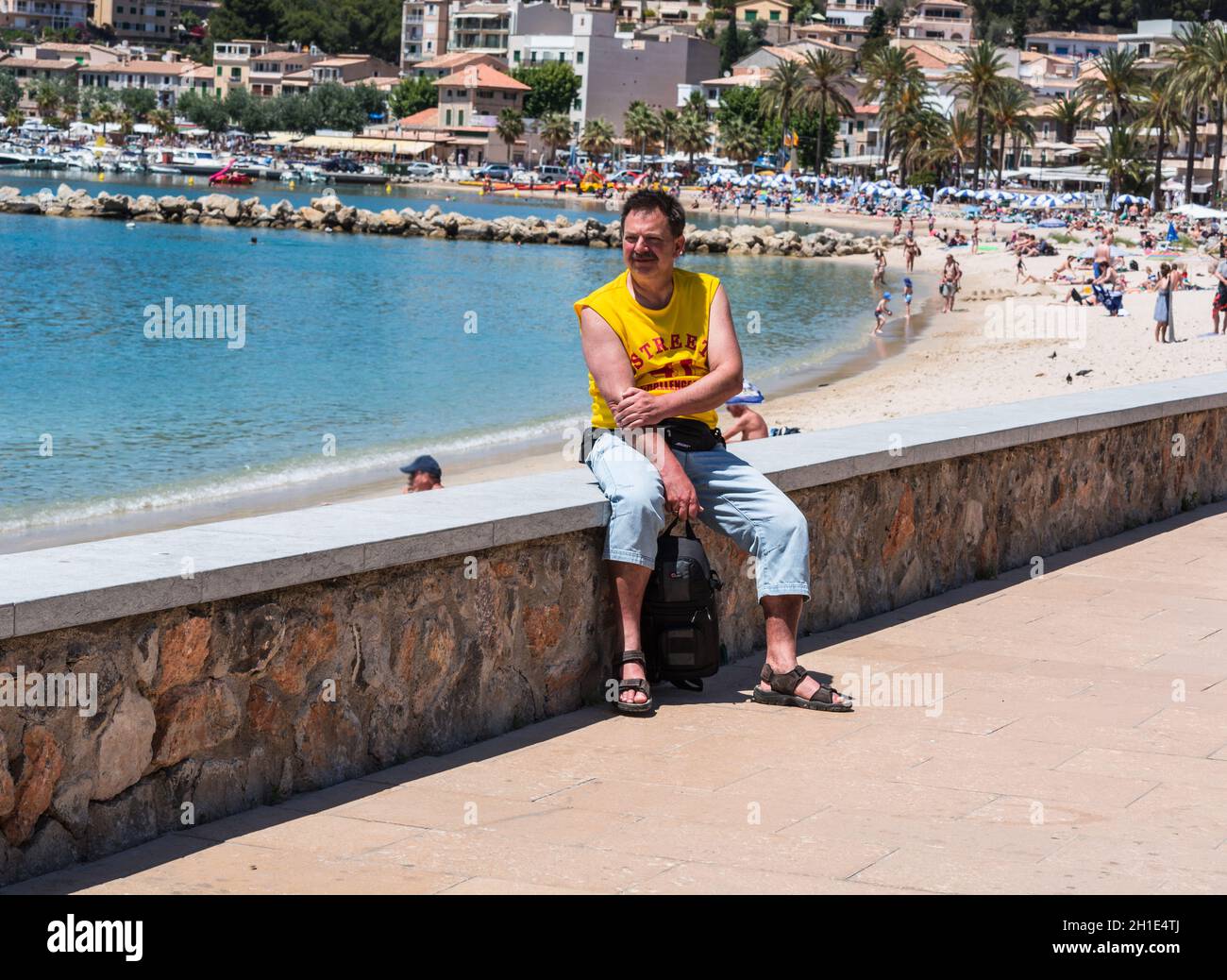Paguera, MALLORCA, SPAIN - JULY 02, 2016: Paguera, Mallorca, Spain - July 02, 2016: A man sitting in the sunshine on a wall in the background pine for Stock Photo