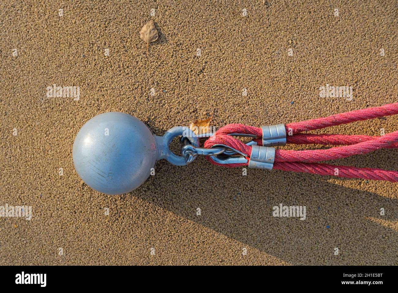Metal fastening and a red rope, on the playground, against the background of a soft surface, outdoors.  Stock Photo