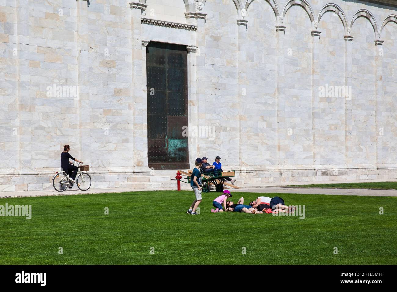 PISA, ITALY - APRIL, 2018: Woman biking next to the Monumental Cemetery at the Square of Miracles in a beautiful early spring day Stock Photo