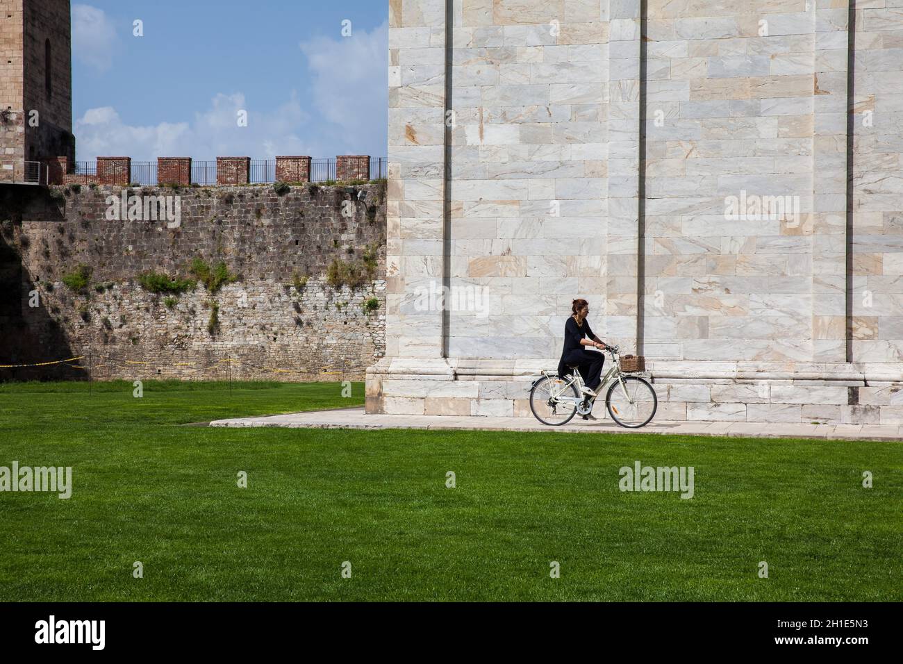 PISA, ITALY - APRIL, 2018: Woman biking next to the ancient walls of Pisa and Monumental Cemetery at the Square of Miracles in a beautiful early sprin Stock Photo