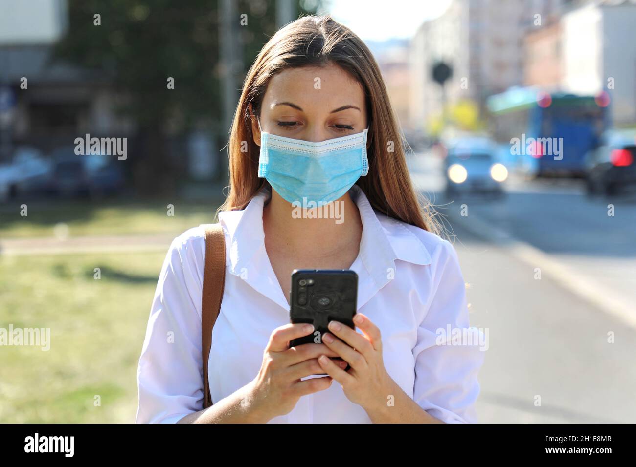 COVID-19 Pandemic Coronavirus Young Woman Wearing Surgical Mask Using Smart Phone App in City Street to Aid Contact Tracing in Response to the 2019-20 Stock Photo