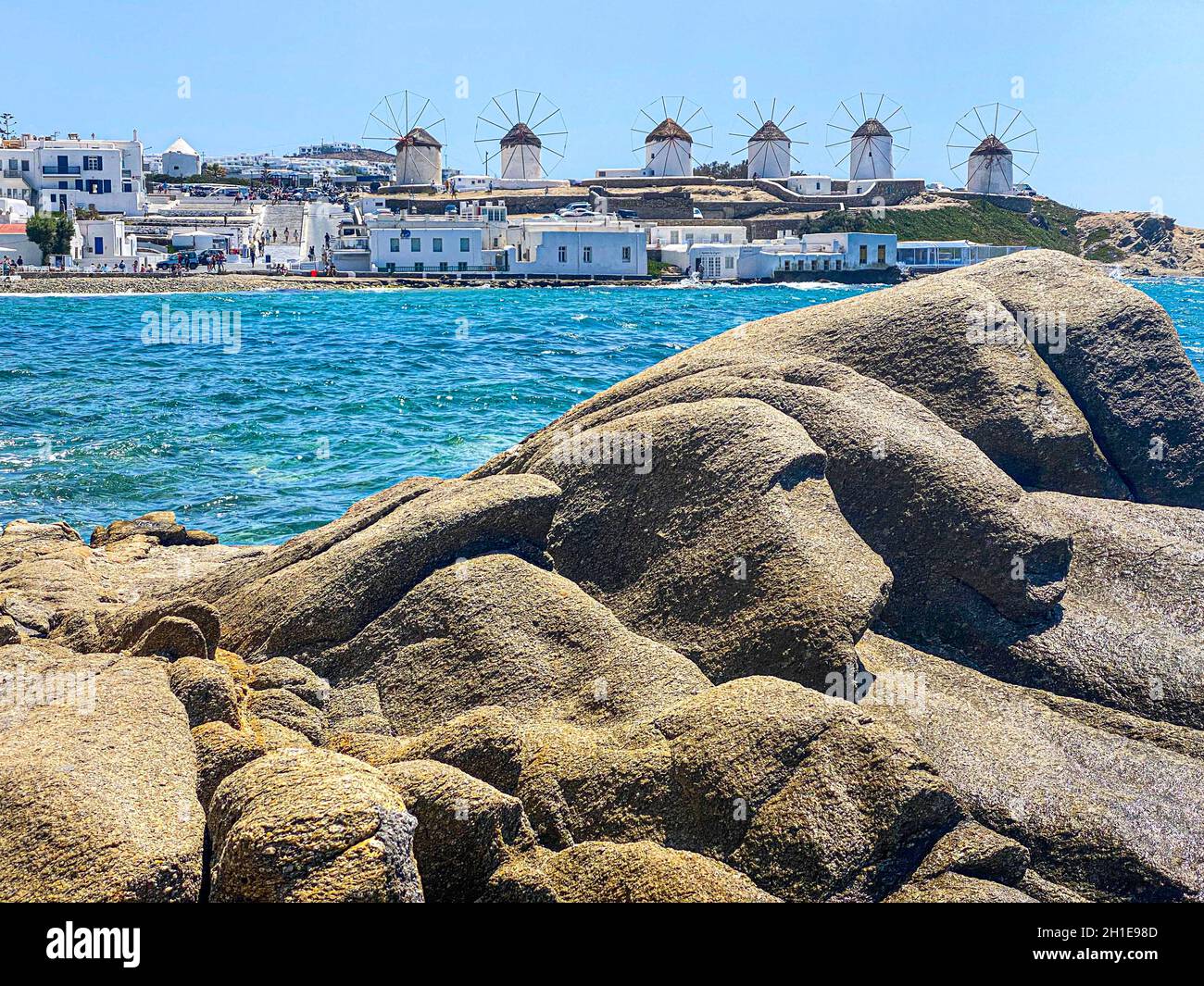 Mykonos windmills in a row on background, rocks on beach on foreground, Greece Stock Photo