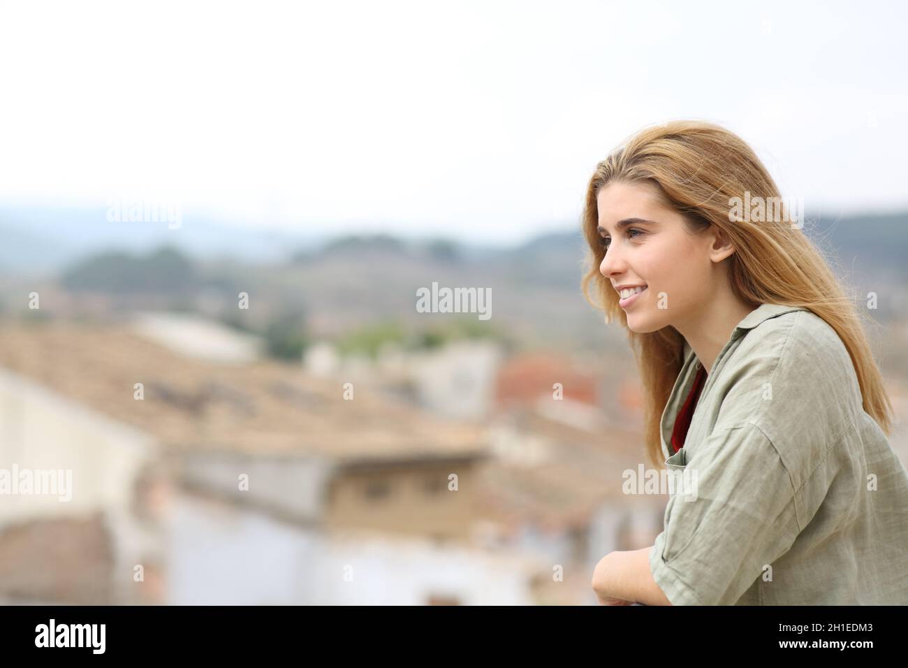 Happy teen girl looking away from balcony in a town Stock Photo