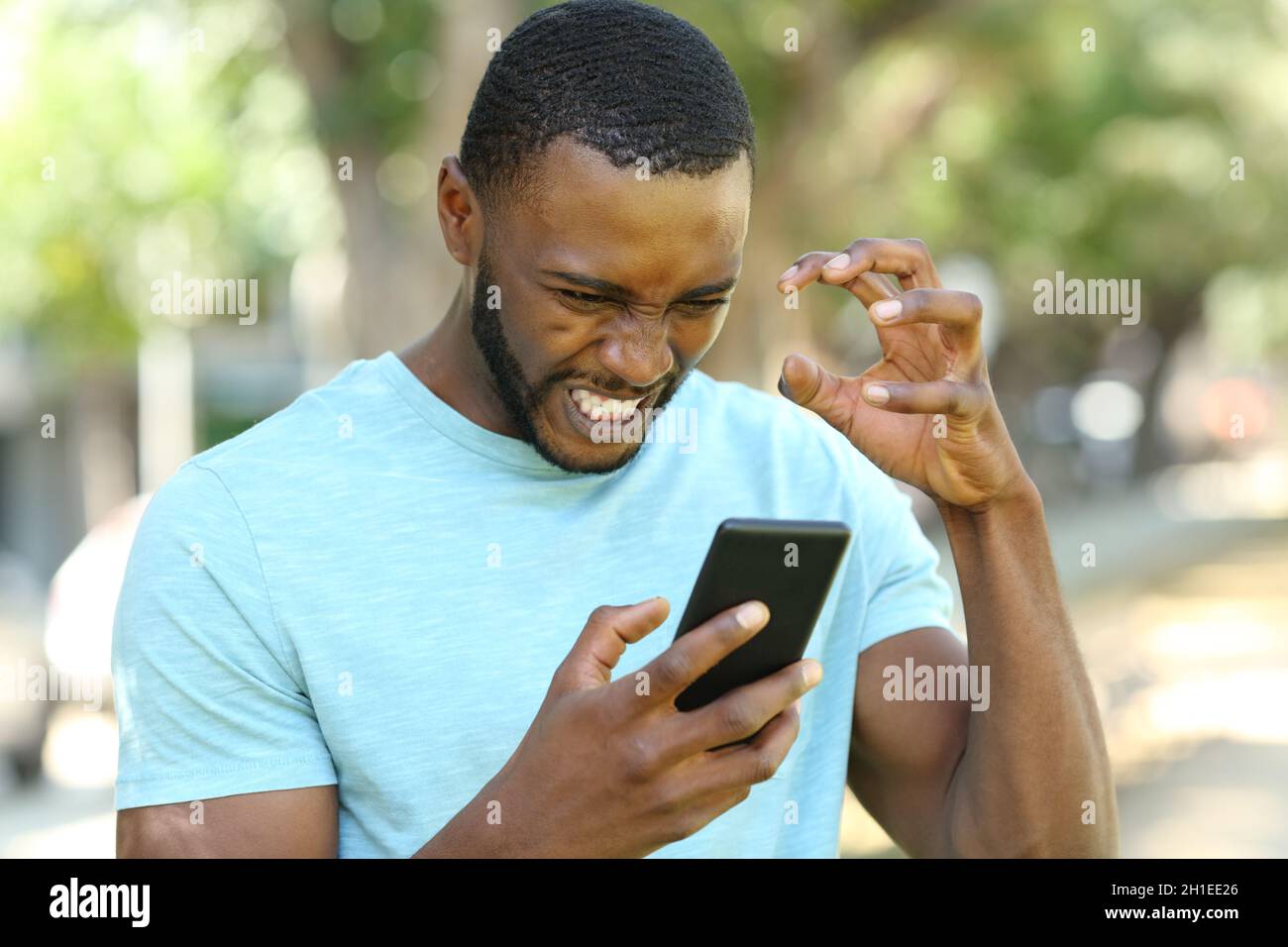Angry man with black skin checking smart phone content in a park Stock Photo
