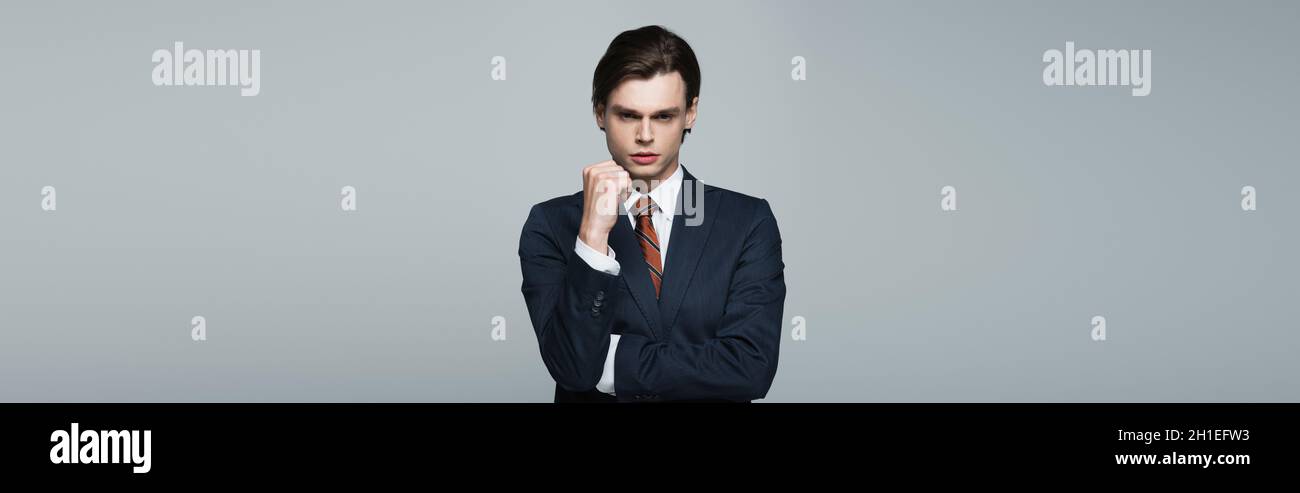 young androgynous businessman in suit posing isolated on grey, banner Stock Photo