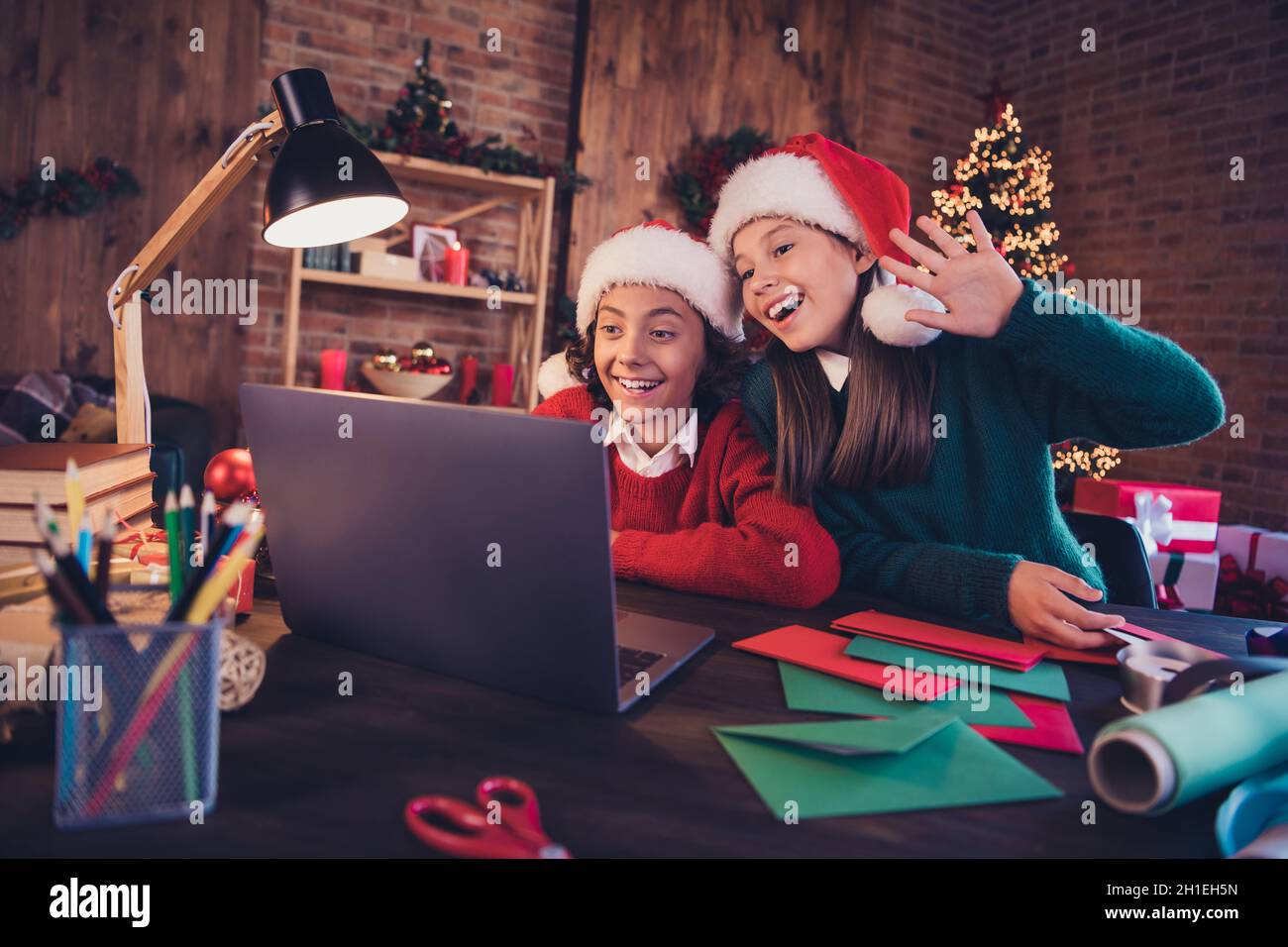 Portrait of cheerful friends preparing event creating advent atmosphere noel using laptop calling waving hello at loft home indoors Stock Photo