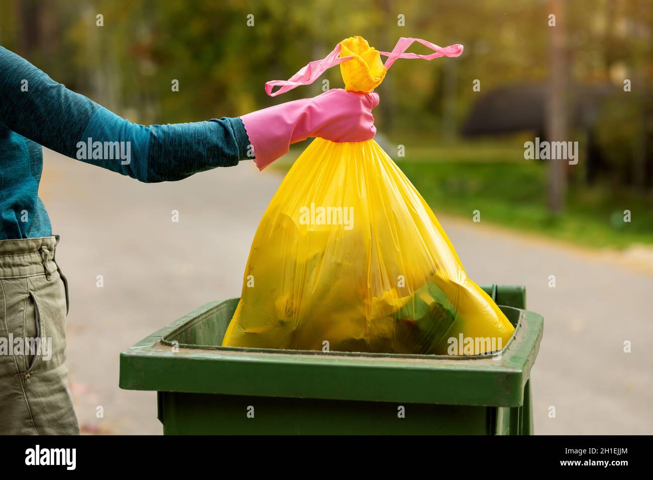 hand put a yellow plastic unsorted garbage bag into trash bin. household waste Stock Photo