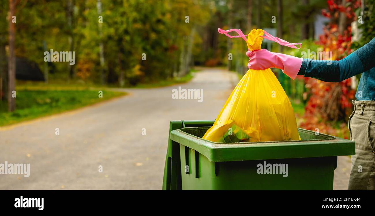 household waste - hand insert yellow plastic unsorted garbage bag into trash bin on the street. copy space Stock Photo