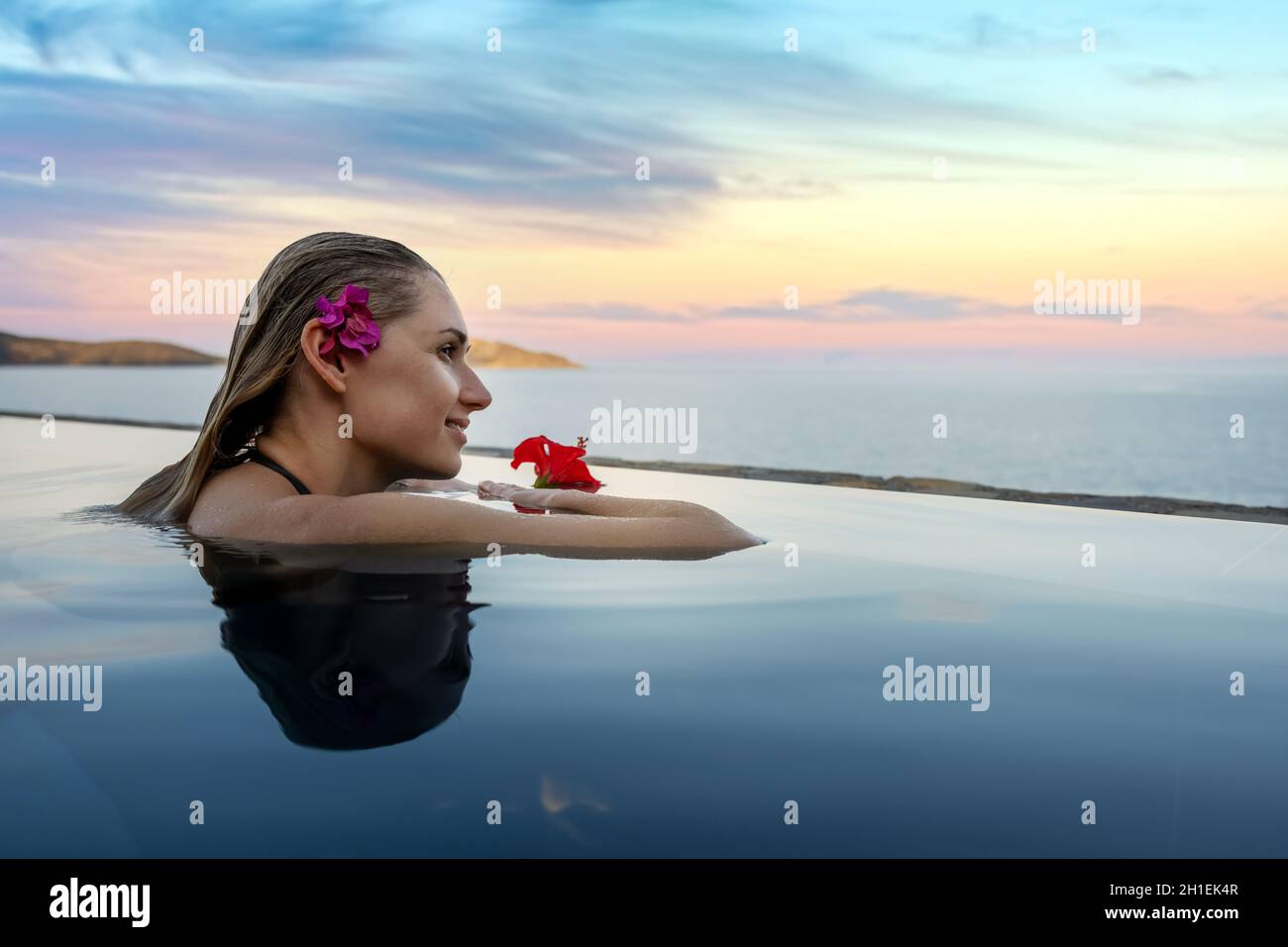 luxury resort vacation - woman with flower in the hair relaxing in infinity swimming pool with sea view. copy space Stock Photo