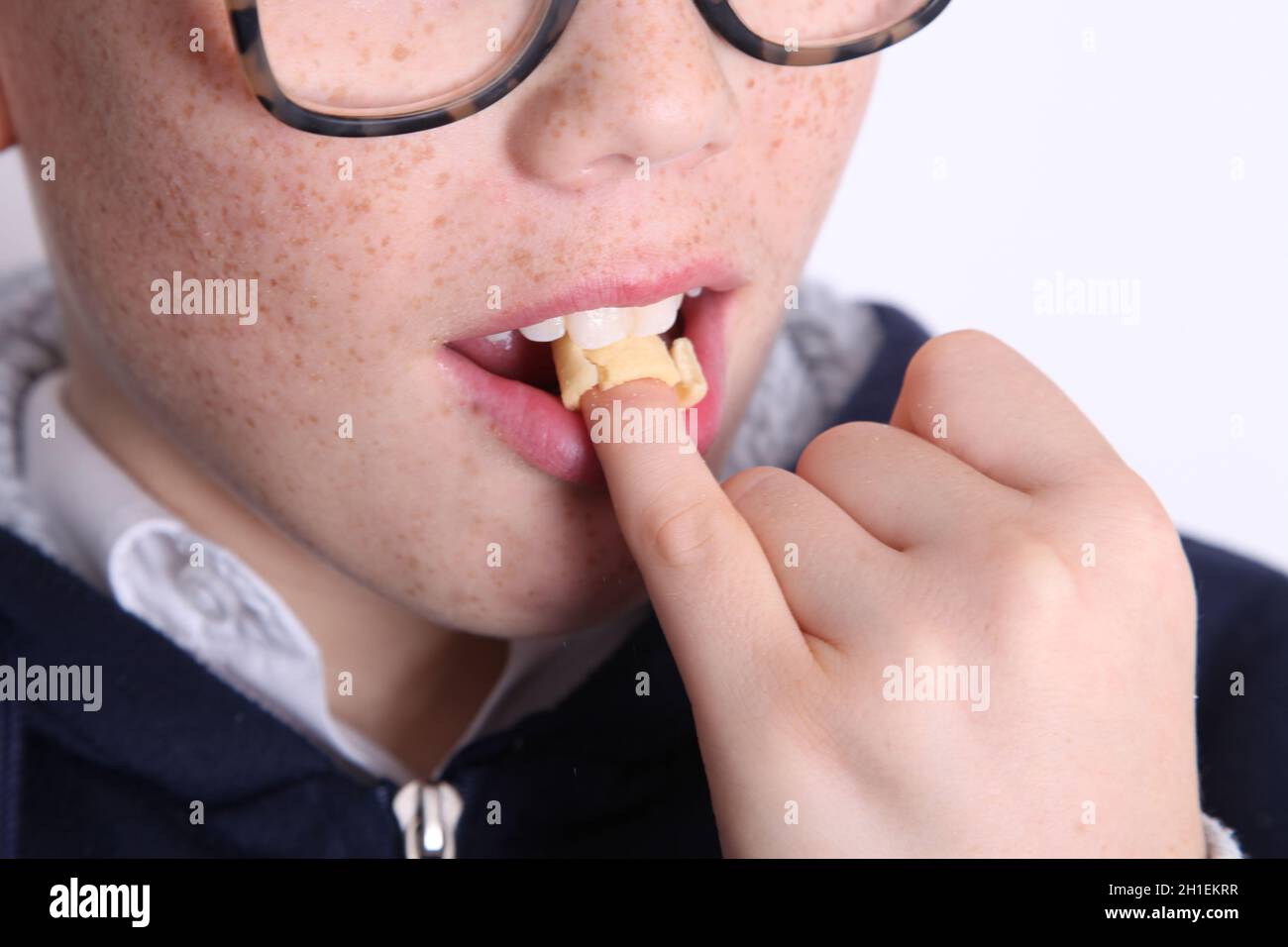 Hula Hoop on finger tip being bitten by freckled boy, close up of mouth and face against white background Stock Photo