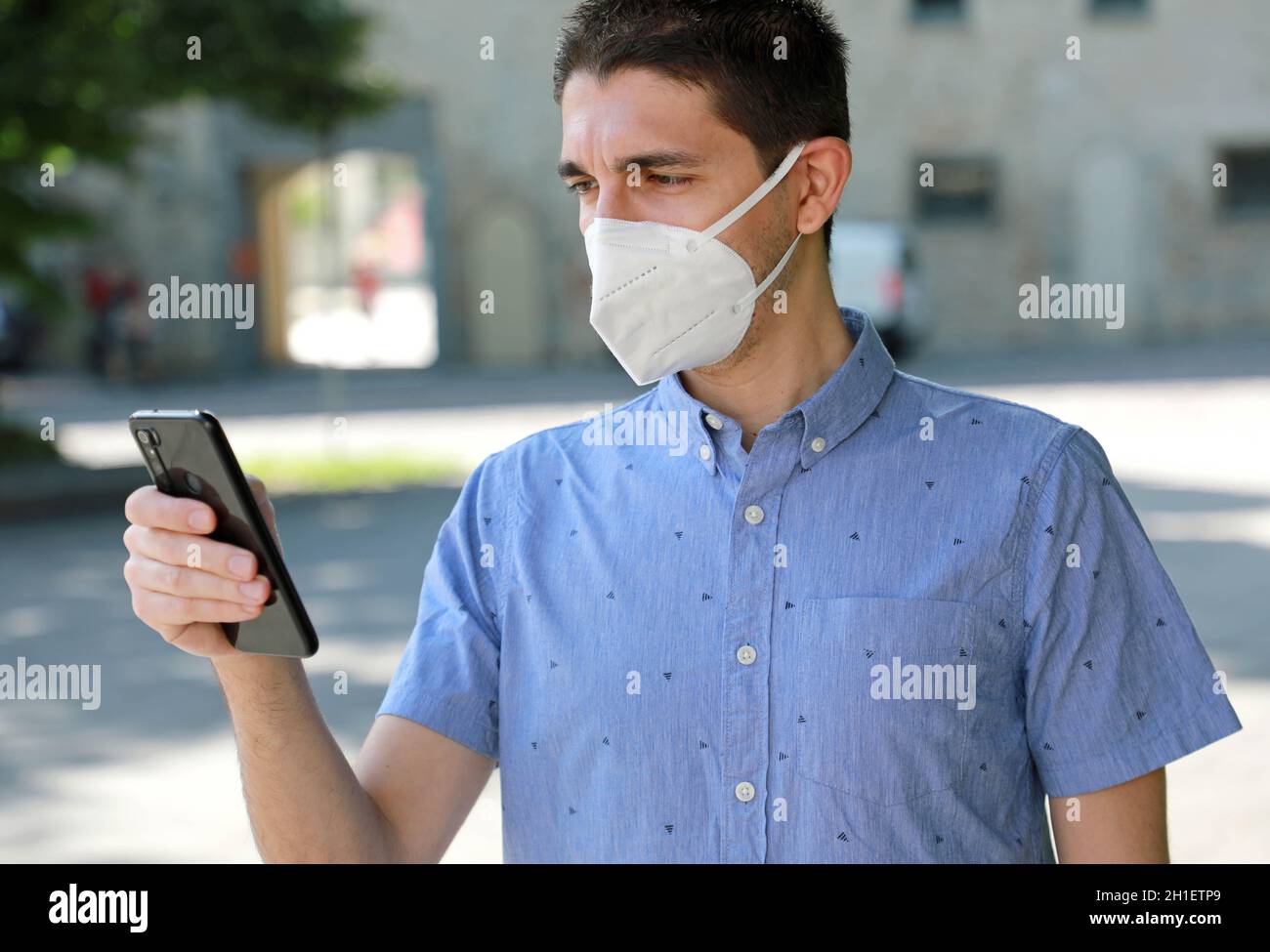 COVID-19 Mobile Application Young Man Wearing KN95 FFP2 Mask Using Smart Phone App in City Street to Aid Contact Tracing and Self Diagnostic in Respon Stock Photo